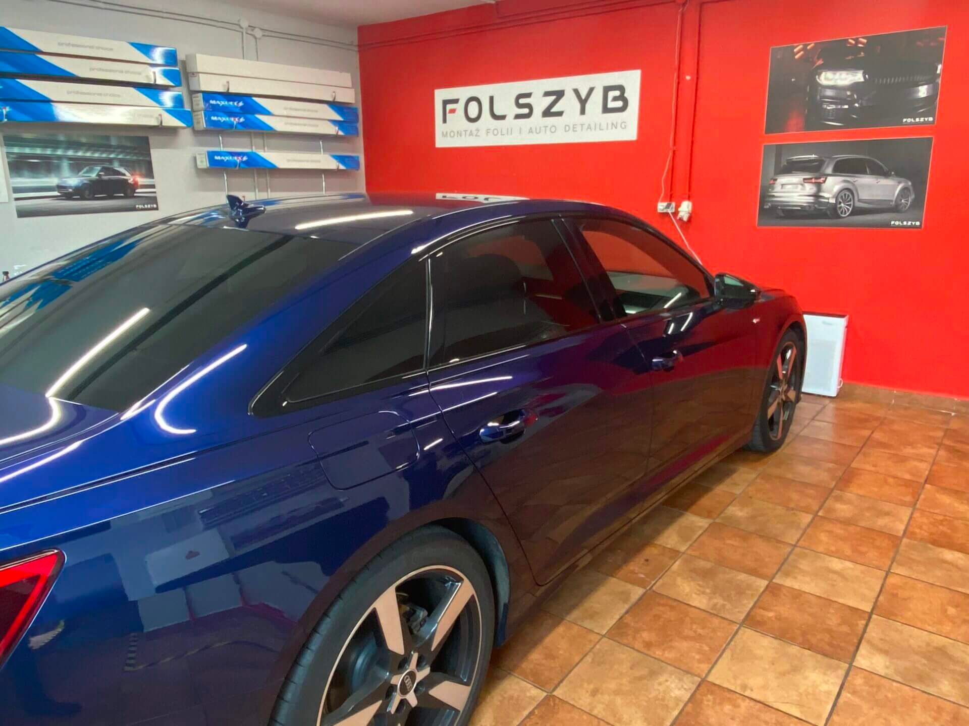 Granatowe Audi A6 z folią na tylnych szybach w hali FOLSZYB; na regale po lewej kartony z rolkami folii